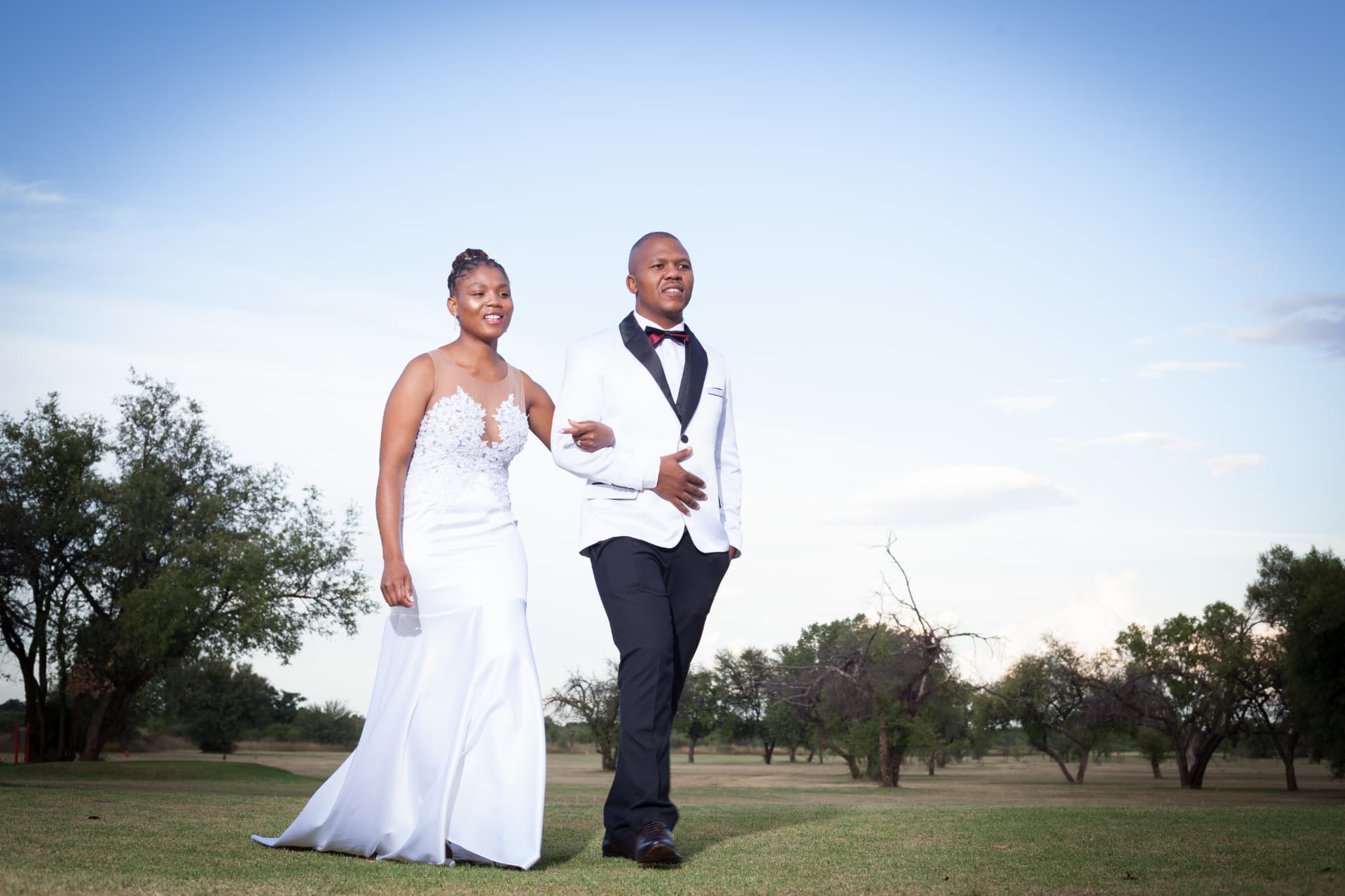 Bride and groom walking on open grassland at golden hour