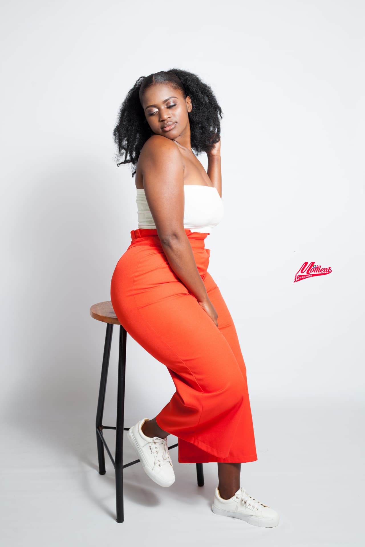 Studio portrait of a model in an orange outfit seated on a stool