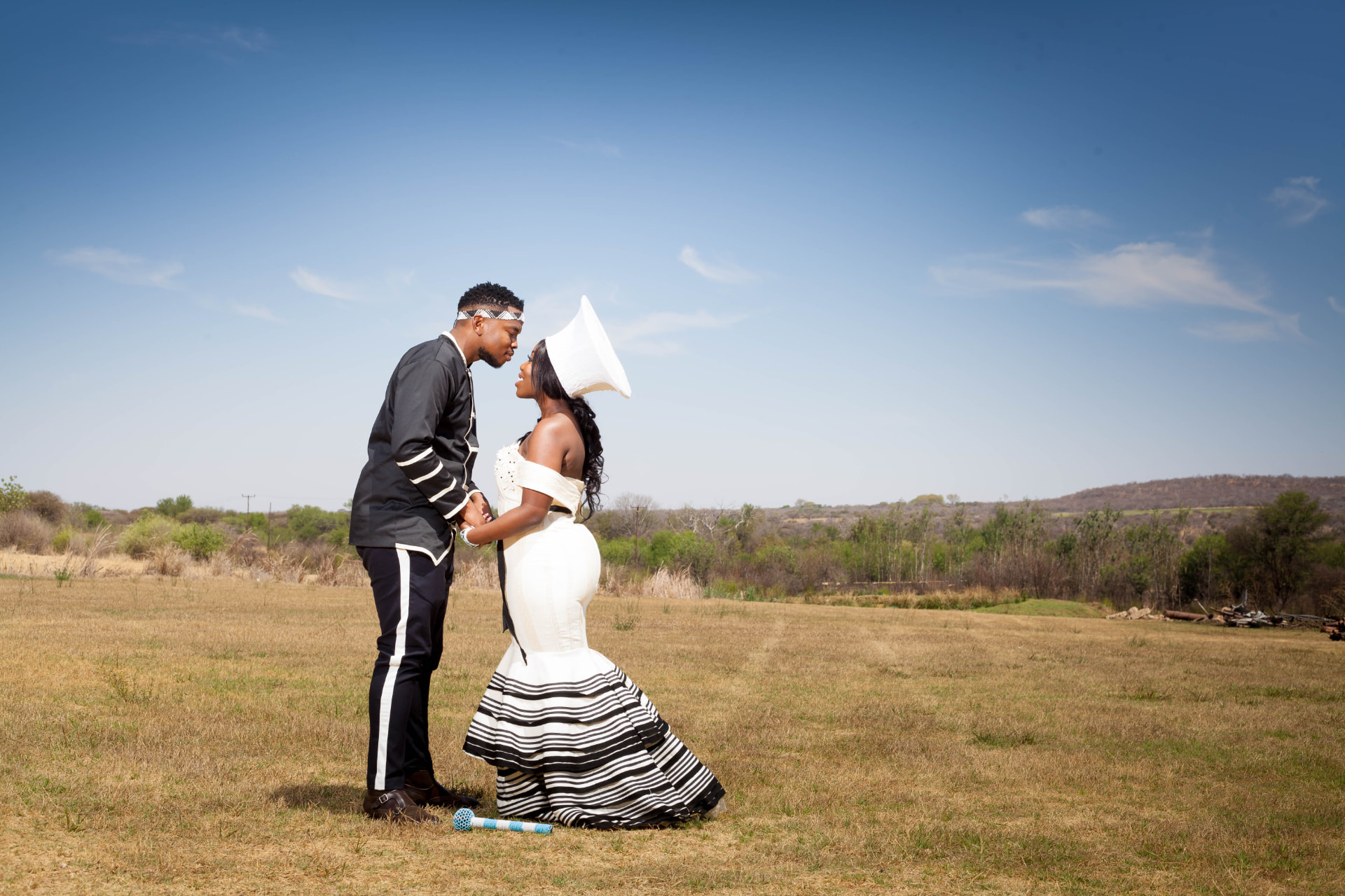 Couple in traditional attire facing each other in an open field under blue sky